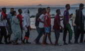 Migrants who have remained in Ceuta queue on the beach outside a food distribution point. In the background are the Spanish mainland and the Rock of Gibraltar. (© picture alliance / AP Photo/Antonio Sempere)